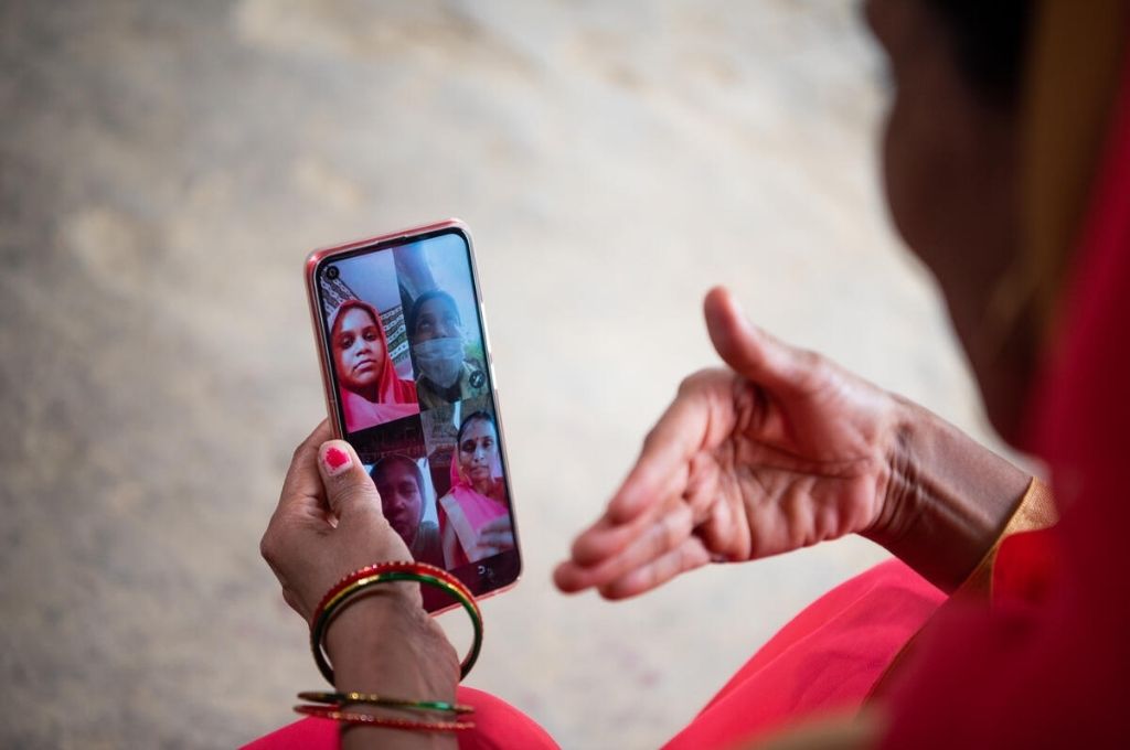 एक आंगनबाड़ी कार्यकर्ता टेलीकाउन्सेलिंग के लिए लाभार्थी महिलाओं के एक समूह को स्मार्टफोन से वीडियोकॉल करते हुए_गेट्स आर्काइव/सौम्या खंडेलवाल-कोविड-19 संचार