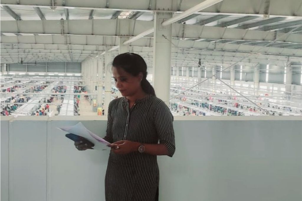 शैला, गुड बिजनेस लैब में काम करने वाली एक गणनाकर कपड़े के एक कारखाने में खड़े होकर रिपोर्ट पढ़ रही है- सर्वे कर्नाटक