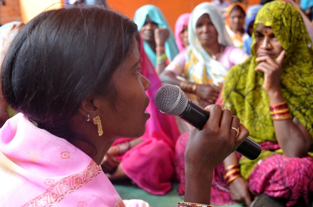 गुलाबी साड़ी में माइक लिए एक महिला महिलाओं के समूह से बात करती हुई-भारत की राजनीति महिला