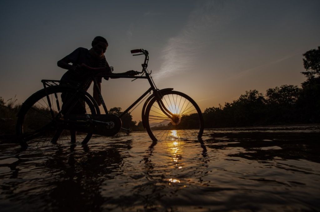 आदमी अपनी साइकिल को पानी के पार ले जा रहा है-प्रवासी मज़दूर