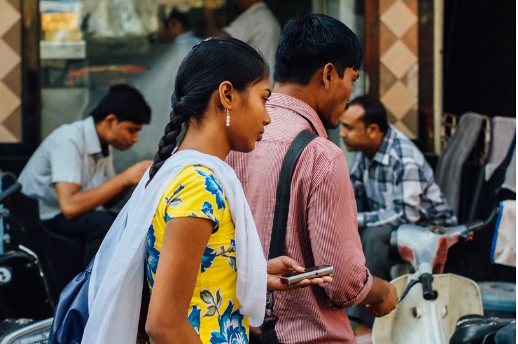 भारतीय महिला एक पुरुष के पीछे स्मार्टफोन लिए खड़ी है-भारतीय महिलाएं रोज़गार
