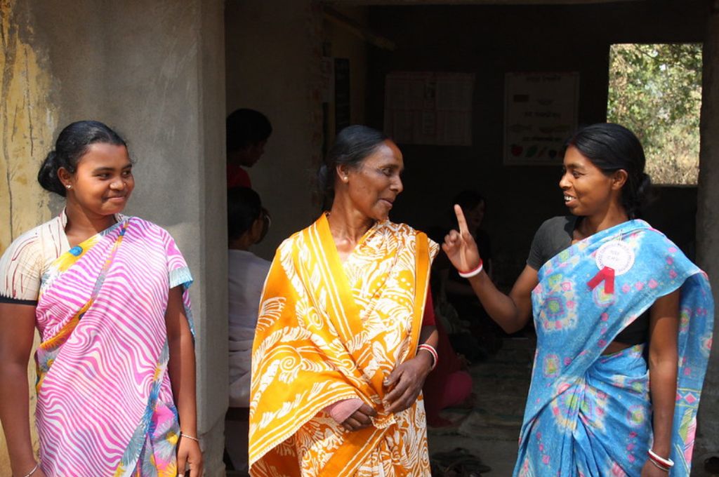 साड़ी पहने तीन महिलाएं मुस्कुरा रही हैं और एक दूसरे से बात कर रही हैं-NGO