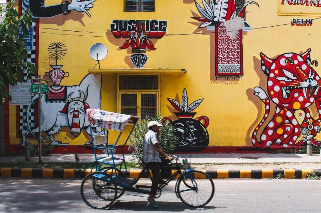एक आदमी रिक्शा चला रहा है। पीछे एक पीले रंग की दीवार पर ग्राफिटी है और न्याय लिखा हुआ है-मानसिक स्वास्थ्य