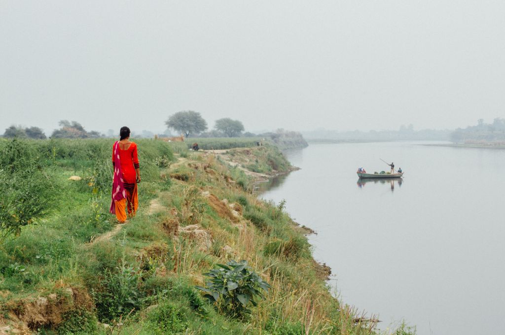 नदी के किनारे चलती महिला किसान-ज़मीन अधिकार