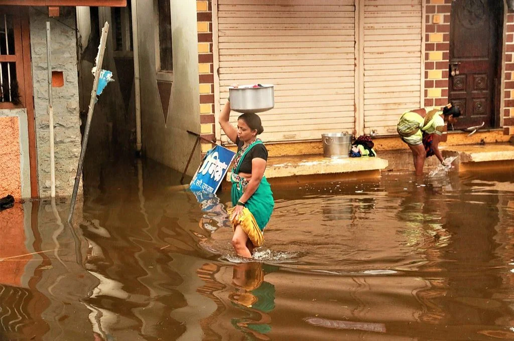 बाढ़ के कारण सड़क पर हुए जलजमाव में चलती हुई एक महिला_महिला जलवायु परिवर्तन
