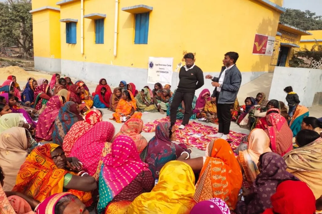 जमीन पर घेरे में बैठी महिलाओं के समूह को संबोधित करते दो पुरुष_आपराधिक न्याय प्रणाली