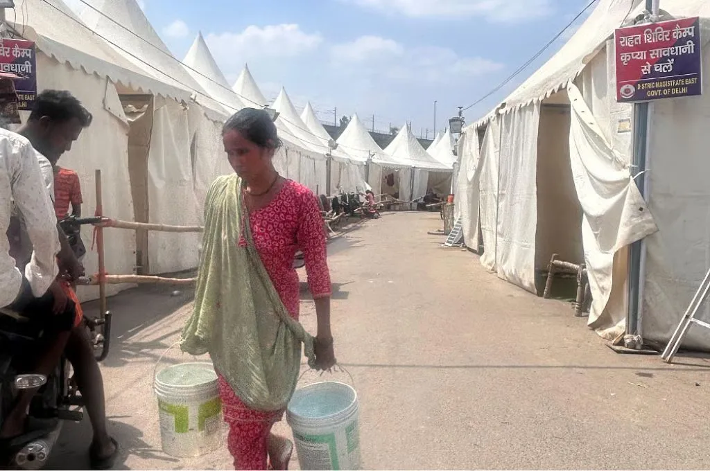 राहत शिविर में पानी ले जाती एक महिला_यमुना राहत शिविर