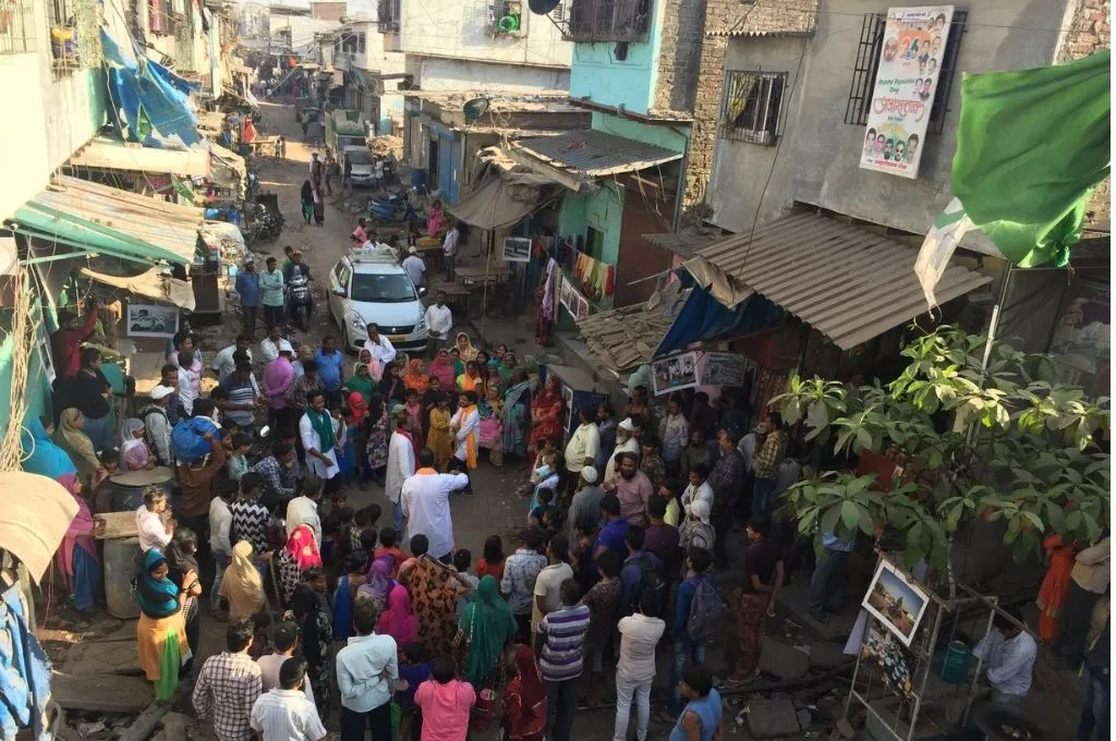 एक शहरी गली जिसमें दोनों ओर छोटे घर और दुकानें है और कुछ लोग बीच में चर्चा करते हुए_पानी का अधिकार