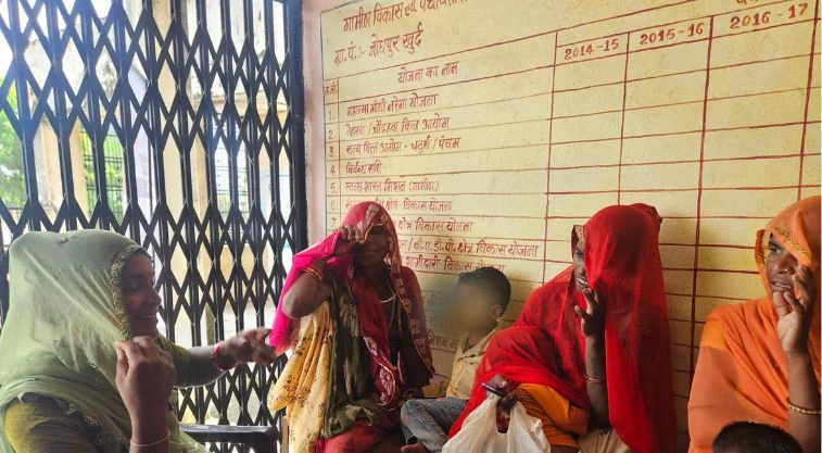 महिलाओं का एक समूह दीवार के सहारे बैठा हुआ है_वीबी-जी राम जी
