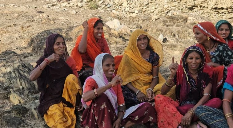 महिलाओं का एक समूह जनसभा जैसे वातावरण में अपने हाथ उठाते हुए_वीबी-जी राम जी