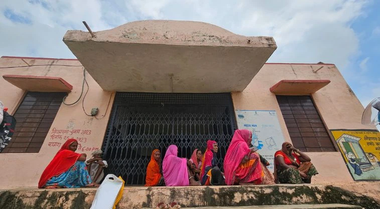 महिलाओं का एक समूह किसी सरकारी भवन के द्वार पर बैठा हुआ है_वीबी-जी राम जी