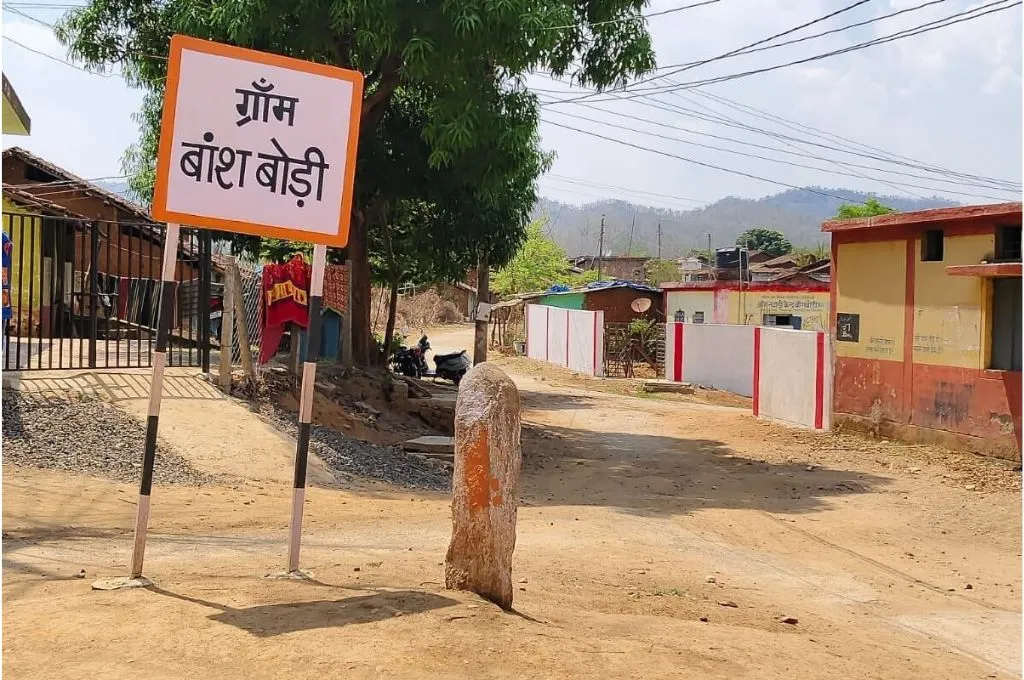 एक गांव के साइन बोर्ड के पास खड़ी ग्रामीण महिला_वन ग्राम