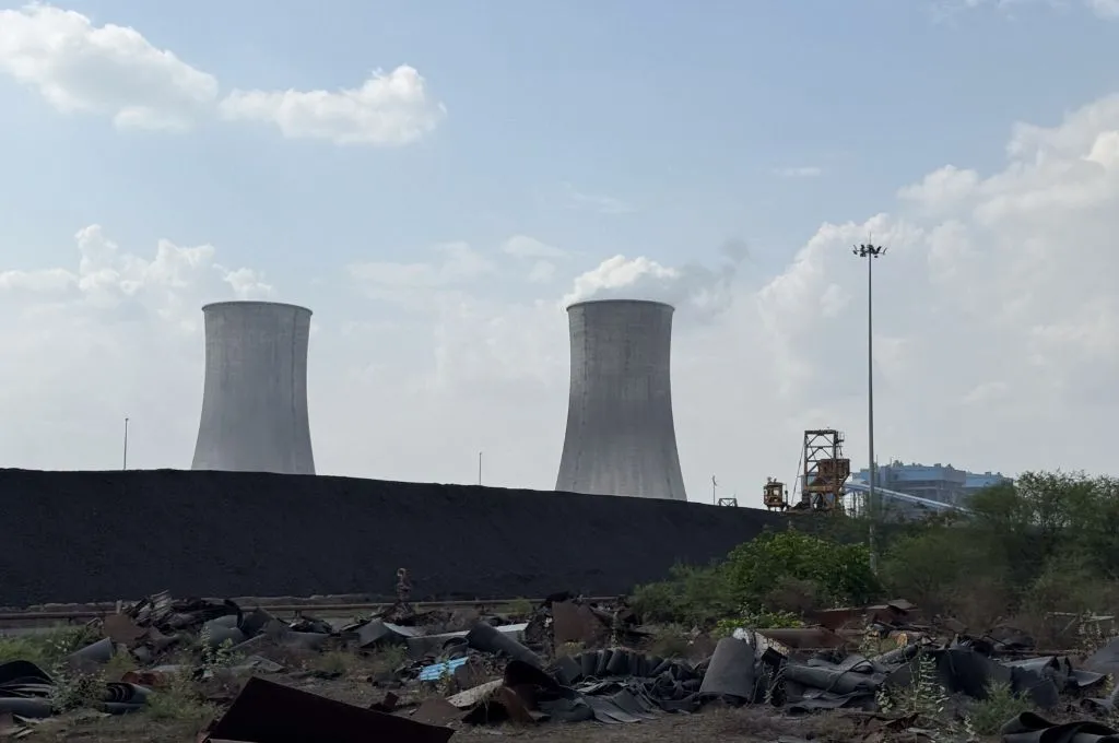 दीवार की एक तरफ़ कुछ कचरा और दूसरी तरफ़ पावर प्लांट फैक्ट्री की दो चिमनियां_छबड़ा थर्मल पावर प्लांट
